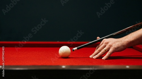 Man lines up a shot with a cue stick on a red billiard table preparing to strike the cue ball with precision in a game of pool