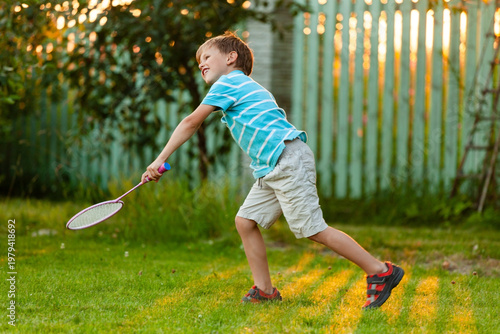 A young boy engaged in active badminton play outdoors on a sunny summer day. Dynamic movement, coordination, and fun leisure time during holidays in a green park.