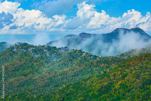 Green mountains contrast with the blue sky and a light mist.