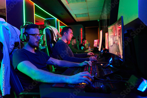 Competitive Gamers Playing Multiplayer PC Games In Neon-Lit Esports Gaming Arena With Headsets