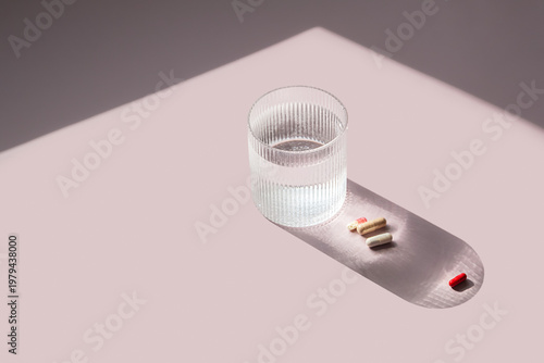 Glass of water and supplement capsule on pastel background. Daily pill intake and medical treatment routine.
