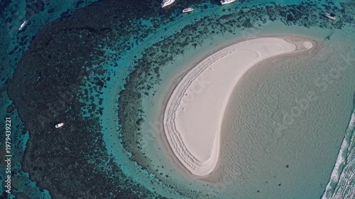 Aerial view of a sandy beach island surrounded by turquoise waters and coral reefs, with boats anchored nearby, showcasing the natural beauty of a coastal landscape