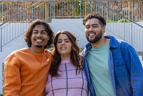 Slika na platnu Three friends standing on concrete steps by metal railings, smiling and showing
