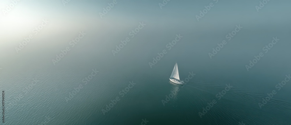 Fototapeta premium Aerial drone view of tiny white sailboat on glassy calm ocean with soft pastel mist and pale horizon