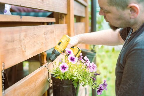 Wallpaper Mural Man fixes wooden fence with drill, adding a flower pot Torontodigital.ca