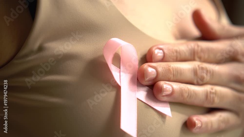 Close-up shot of female hand touching pink breast cancer awareness ribbon on shirt, symbolizing medical support and solidarity in October.