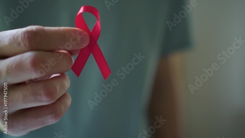 Detailed shot of man's hand giving red awareness ribbon to woman's hand representing united support for HIV positive people.