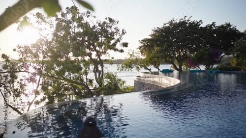 Wallpaper Mural A tranquil pool by the beach during sunrise with warm light reflecting on the water. Green trees frame the scene while the ocean and shoreline create a peaceful tropical coastal atmosphere. Torontodigital.ca