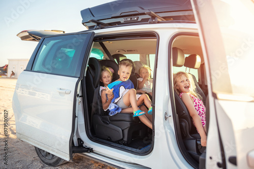 Konstfotografi Group of four cute adorable little happy caucasian children enjoy having fun sit in minivan going to sea beach road trip on hot summer day