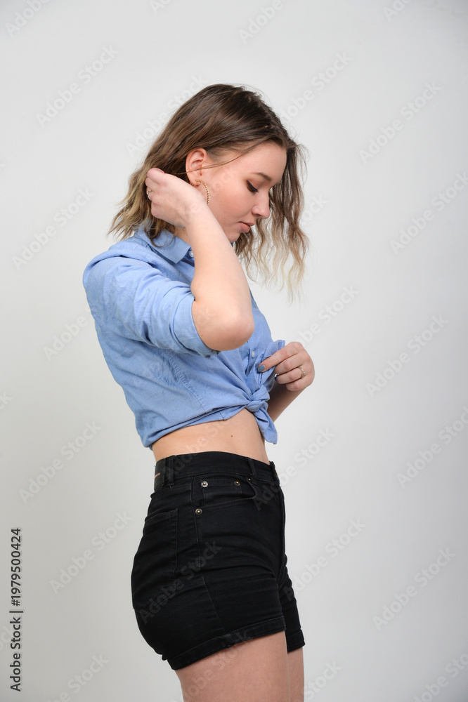 Naklejka premium Junge Frau im bauchfreien Denim-Outfit, skinny Figur und lässiger Look, nachdenkliche Pose, modernes Fashion- und Lifestyle-Porträt