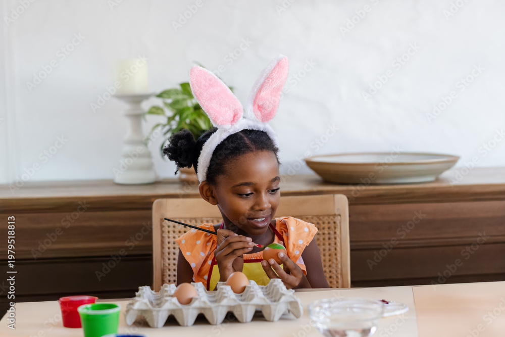 Obraz premium African American female child painting Easter egg at wooden table holding paintbrush and egg