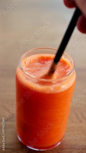 Fresh orange juice being stirred into a glass with a straw creating foam and bubbles