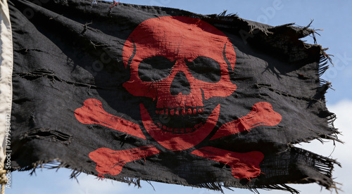 Weathered black pirate flag with red skull and crossbones symbol waving against blue sky. Tattered fabric shows authentic wear and frayed edges. For maritime, adventure, and nautical themed projects.
