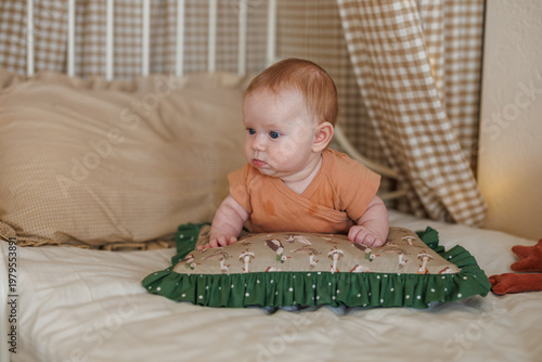 A baby lies on a green ruffled pillow on a white bed. The baby is looking to the side