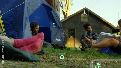 Diverse friends sitting at grassy campsite by cabin monitoring AR data near blue tent