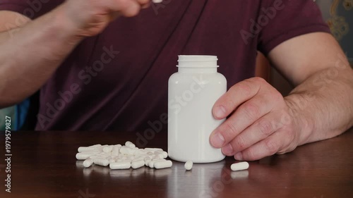 Man putting white medical capsules into a white plastic bottle, process of packing medicine or dietary supplements.