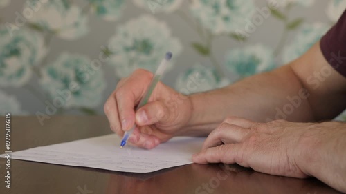 Close-up of a person's hands writing with a blue ballpoint pen on a blank white sheet of paper