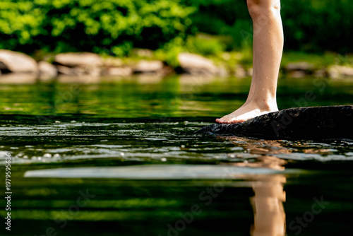 Foto Bare, wet legs and feet of a person standing on a large rock with a perfect mirror-like reflection visible in the  water of the river below, suggesting summer swimming