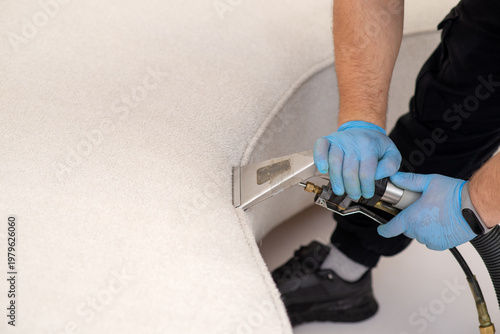 Professional dry cleaning of a white curved sofa using a specialized extraction upholstery tool.