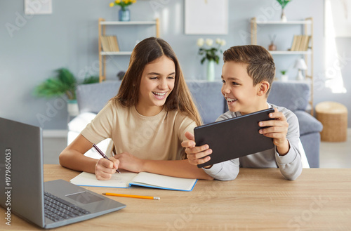 Schilderij op canvas Two children are happily doing their homework and having fun using modern gadgets