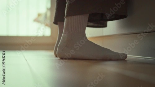 On a tiled kitchen floor near the balcony doors, a housewife-still a girl at heart-stands in white socks, her feet planted firmly as she tends to daily chores, embodying home routine