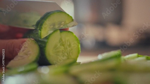 Slicing a fresh green cucumber, a housewife's skilled hands move deftly in a home kitchen. On a bright sunny day, she prepares food with precision, showcasing the art of culinary preparation