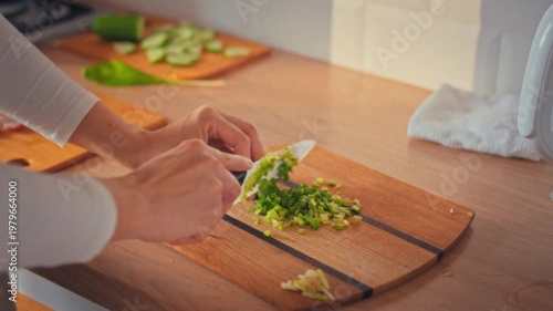 A housewife's skilled hands chop fresh greens with a sharp kitchen knife on a worn cutting board, preparing ingredients for a healthy salad, showcasing her culinary expertise in food preparation