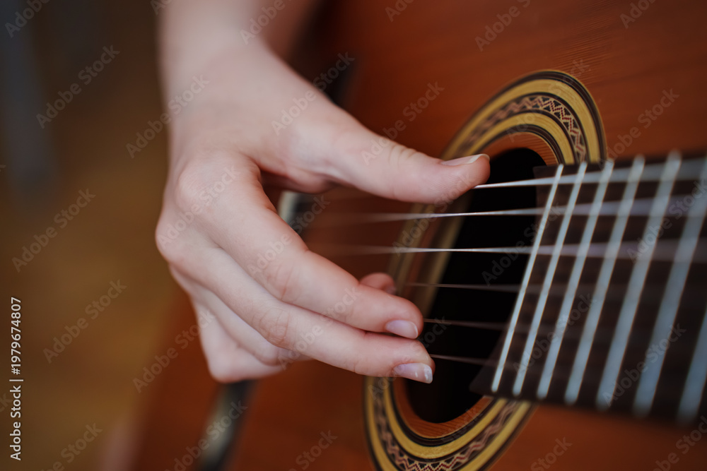 Fototapeta premium Person plays guitar with fingers on strings indoors in warm light