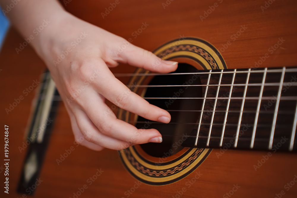 Fototapeta premium Girl plays guitar at home in afternoon with focus on hands