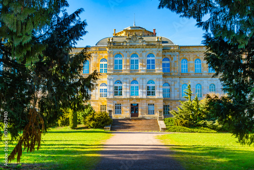 Herzogliches Museum Gotha framed by trees in spring daylight, historic palace facade with symmetrical architecture, green park lawn and clear blue sky, cultural museum landmark in Thuringia, Germany