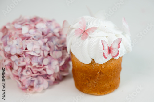Easter cake with white icing and pink butterfly decorations with soft hydrangea flowers in background, delicate spring dessert on light minimal background.
