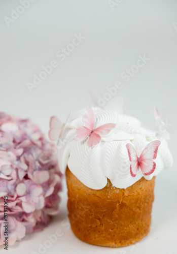 Easter cake with white icing and pink butterfly decorations with soft hydrangea flowers in background, delicate spring dessert on light minimal background.