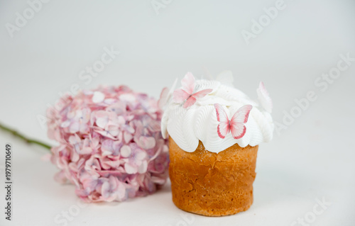 Easter cake with white icing and pink butterfly decorations with soft hydrangea flowers in background, delicate spring dessert on light minimal background.
