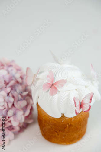 Easter cake with white icing and pink butterfly decorations with soft hydrangea flowers in background, delicate spring dessert on light minimal background.