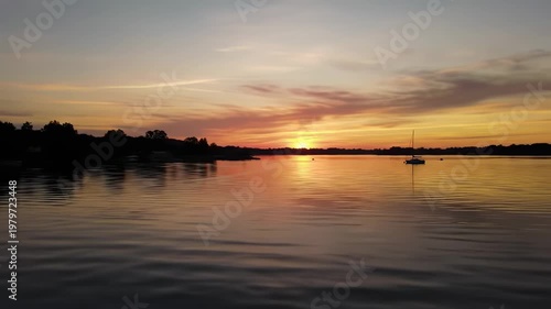 Sunset over a Calm Lake with a Lone Sailboat During Summer Evening