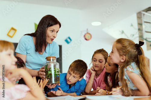 Teacher showing a terrarium to curious elementary students during a hands-on classroom science lesson