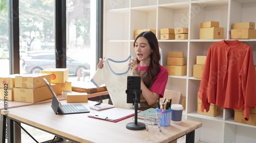 A small startup business run by a young Asian woman working from home, using a laptop for online marketing and preparing packaging for customer orders.