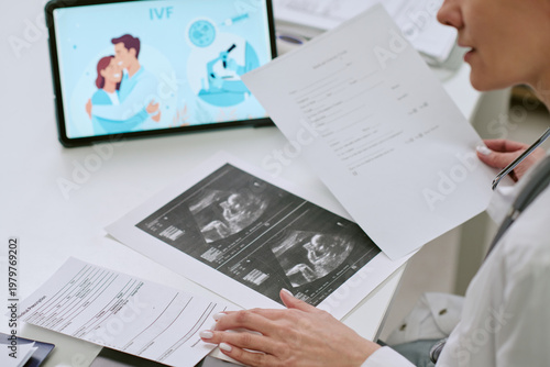 Obraz na plátně Over shoulder view of middle aged woman reviewing ultrasound printouts and IVF p