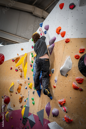 portrait side view of slim white young male indoor rock climber reaching over with right hand to high hold on left side 