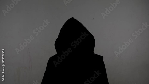 An anonymous silhouette of a person in a hoodie gives an interview against a white, dirty wall