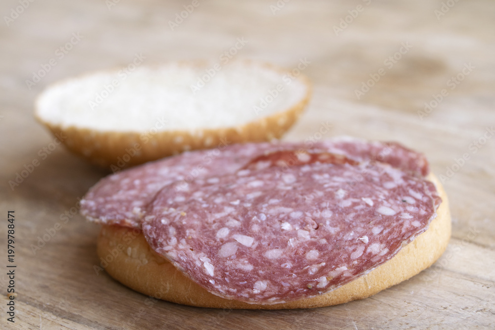 Obraz premium Salami sandwich on sesame seed bun over wooden cutting board