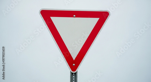 Red and white triangular yield sign against a cloudy sky.