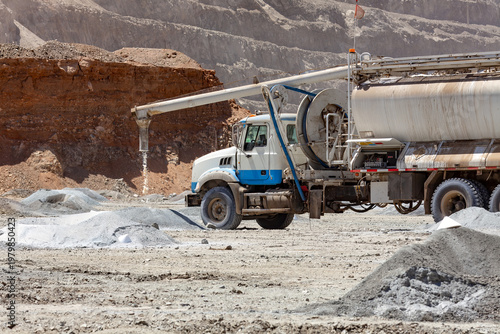 A specialized blasting truck discharges ammonium nitrate granules into a blast holes during explosives preparation at a copper mine.