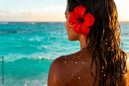 Ocean Dream: A young woman with a vibrant red flower tucked behind her ear gazes at the shimmering turquoise ocean, embodying the spirit of serenity and tropical bliss.