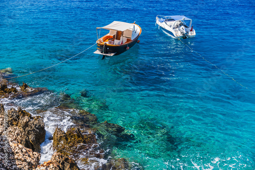 Two small boats gently moored above crystal clear turquoise water beside a ro...