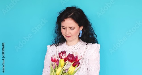 Upset Caucasian Woman Holding Tulip Bouquet and Feeling Bad, Showing Disappointed Facial Expression, Suffering from Flower Allergy or Disliking Gift Gift on Isolated Bright Blue Studio Background