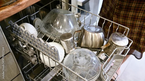Hand placing dirty dishes into dishwasher, kitchen interior with modern design