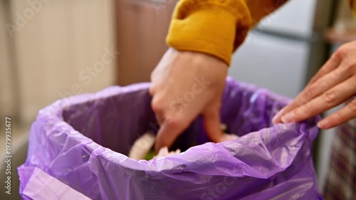 Woman discards flower waste into purple trash bin in kitchen setting