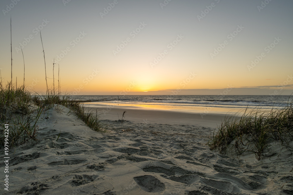 Fototapeta premium Sunset over the beach with sand and grass at the water's edge in the evening
