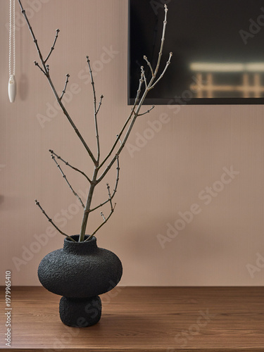 Minimalist interior with dried branches in a dark textured vase on a wooden shelf. Beige ribbed wall background. Japandi style home decor.